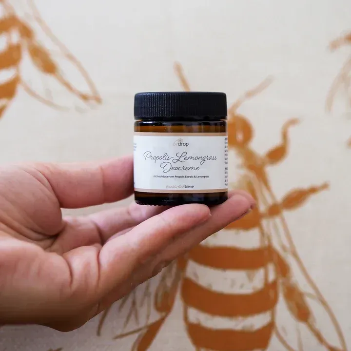 Bedrop Propolis Deo in der Hand einer Person mit einem Bienenbild im Hintergrund